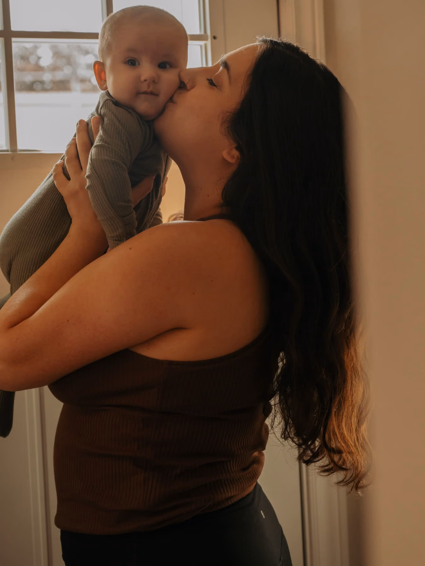 A mother lifts her baby up for a kiss on the cheek.