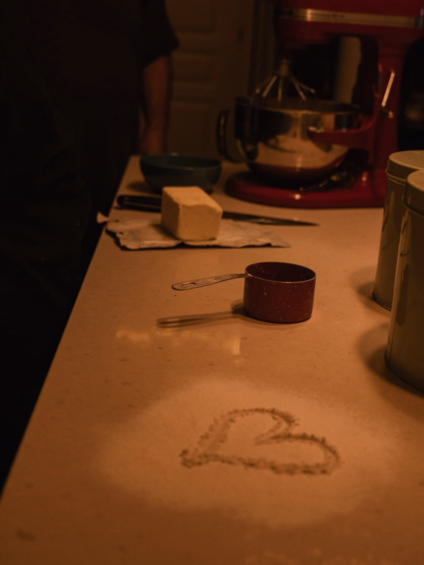 A heart drawn in flour on the counter, butter and a measuring cup beside it.
