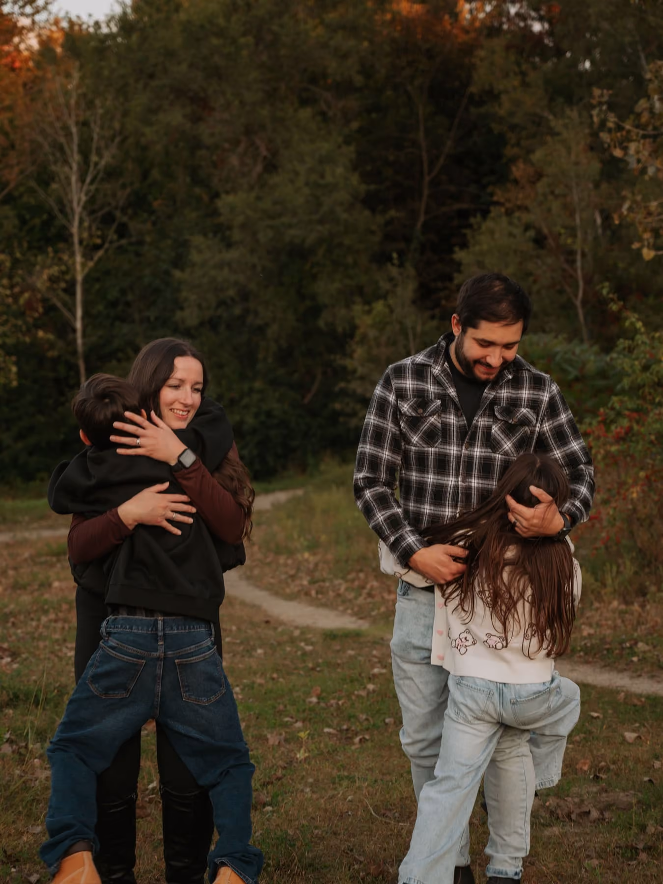 Parents hug their two children in a field at dusk.
