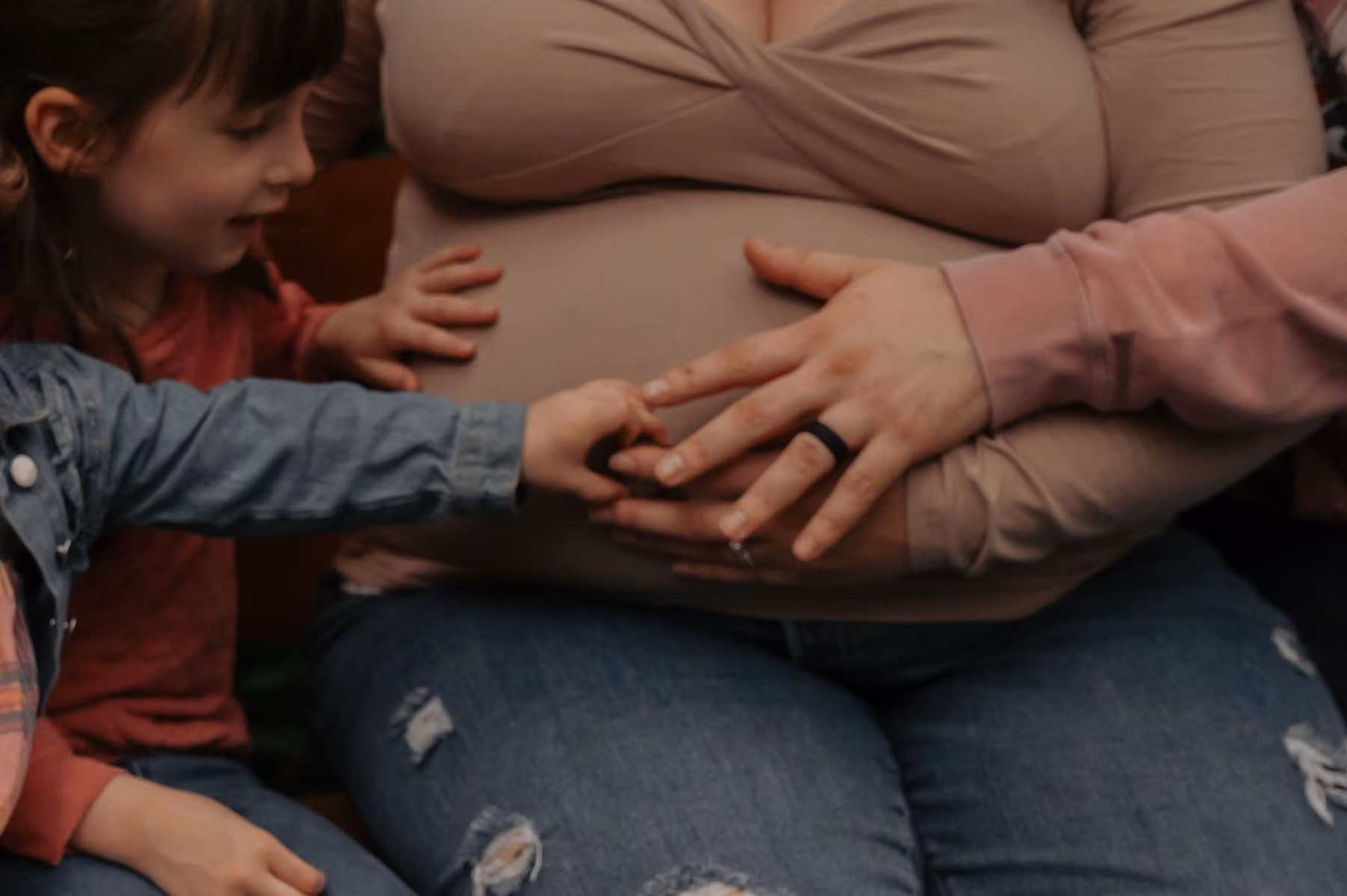 A child’s hand rests on her mother’s pregnant belly.