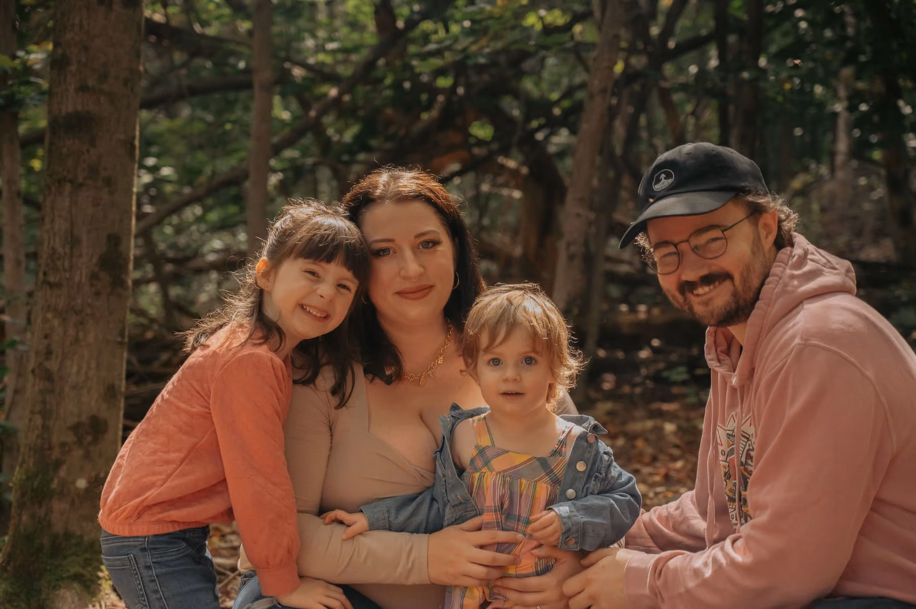 A family of four hug close together among the trees.