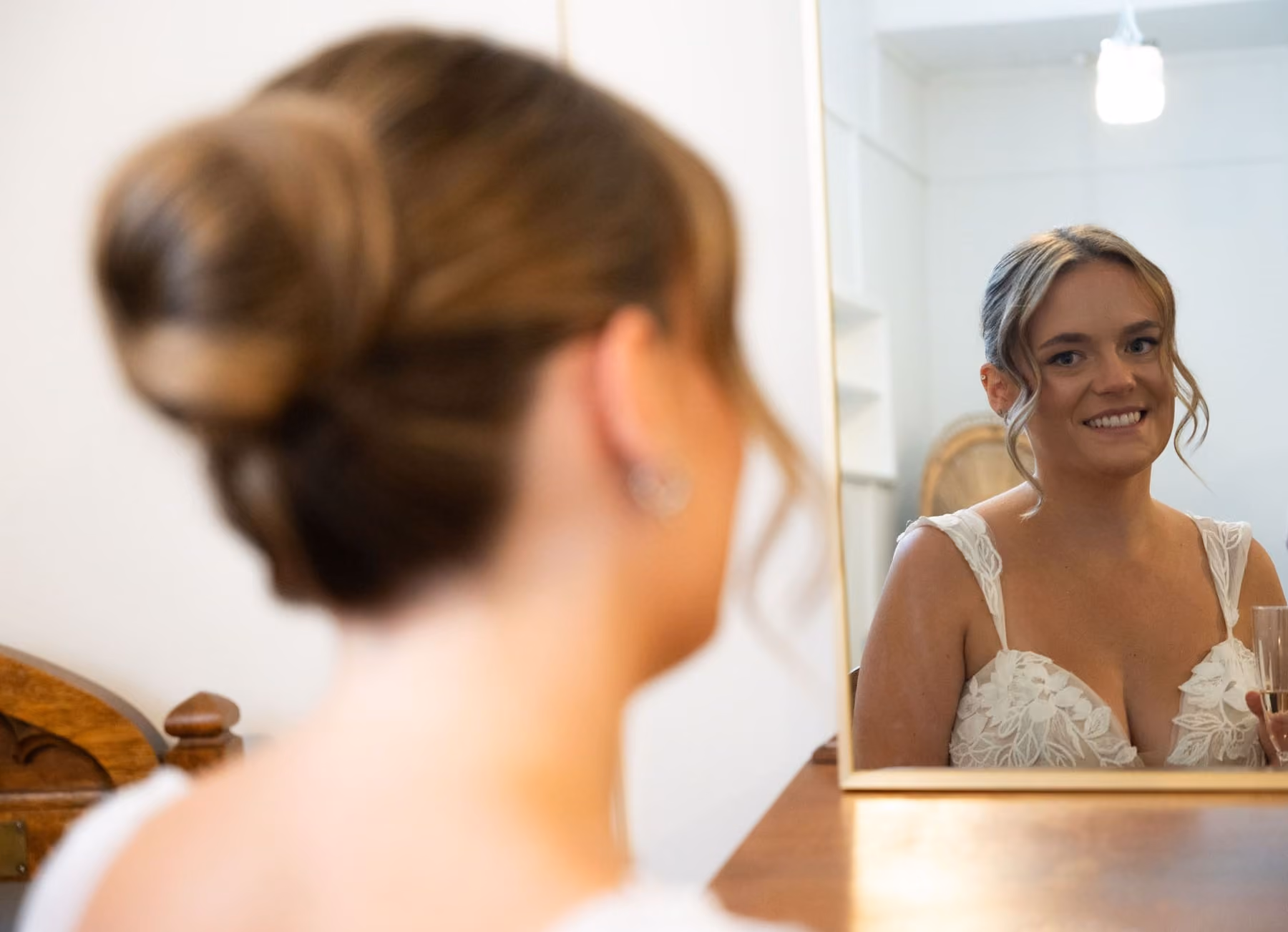 A bride smiles at her reflection in a gold mirror while getting ready.